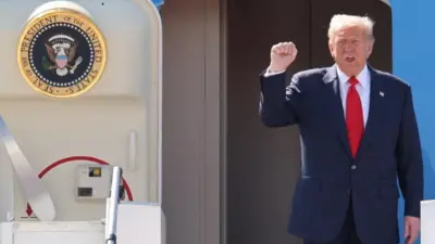 大統領専用機のドア付近でダークスーツ姿のトランプ氏が右手の拳を上げて口を開いている