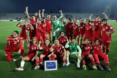 شادی بازیکنان تیم فوتبال زنان که پیراهن‌های سرخ پوشیده‌اند در زمین فوتبال