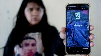 Una mujer con una camiseta con la foto de su esposo desaparecido muestra un celular con la imagen de una camiseta del hombre