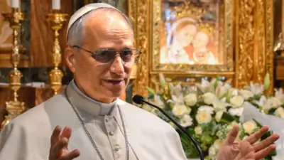 Pope Leo XIV (formerly Robert Francis Prevost) holding his hands up as he talks in front of gold candles and a golden picture frame while he pays a visit to the Shrine of the Mother of Good Counsel in Genazzano, just outside Rome, on 10 May 2025
