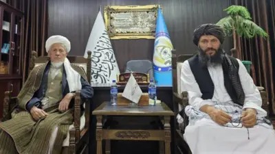 محمد اکبری، معاون شورای علمای شیعه افغانستان در دفتر والی بامیان، در کنار گل‌حیدر شفق نشسته است.