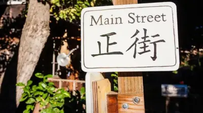 Uma placa com o escrito 'Main Street' e, logo abaixo, o mesmo só que em ideograma chinês