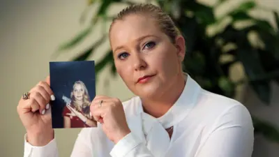 Virginia Giuffre, a blonde woman wearing a white top, holding up a photo of herself as a teenager