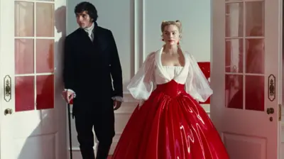 Jacob Elordi in a black suit as Heathcliff and Margot Robbie as Cathy in a white and red PVC dress