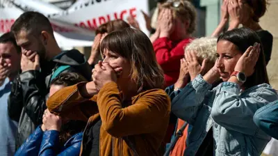 Men and women outside a courthouse in France hold their hands over their mouths in protest