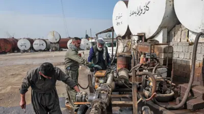 Workers at a market for automotive fuel work on an industrial vehicle next to tanks of oil against a blue sky in Erbil, Iraq, on 17 March.