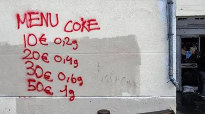 روی دیوار سفید نرخ یک ماده مخدر را با رنگ قرمز نوشته