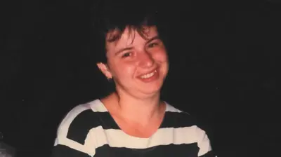 Monika before the crash, she has dark hair and is wearing a black and white striped shirt and is smiling at the camera