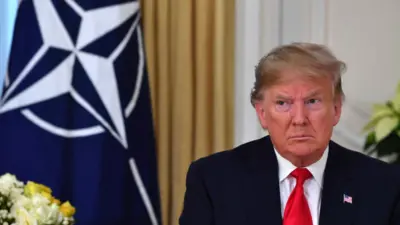 Donald Trump looks unhappy while sitting next to a Nato flag at a meeting in London on 3 December 2019 during his first term as US president.