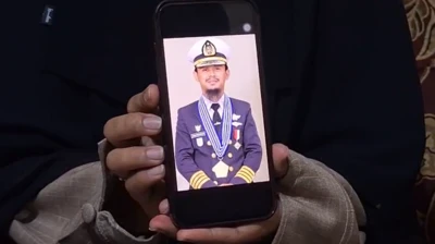 Tangan Santi Sanaya sedang menunjukkan foto suaminya, Ashari Samadikun dari ponselnya. Dalam foto itu Ashari sedang menggunakan seragam seorang nakhoda lengkap dengan topinya.