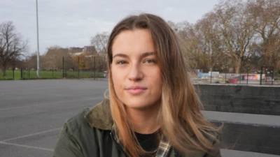 Uzun açık kahverengi saçlı 24 yaşındaki Kaitlin, bir netbol sahasındaki bankta oturmuş kameraya bakıyor.
