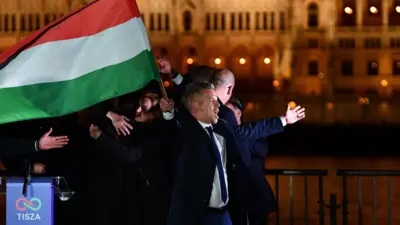 Péter Magyar, lider proeuropejskiej konserwatywnej partii TISZA, macha narodową flagą nad brzegiem Dunaju z budynkiem parlamentu w tle podczas wieczoru wyborczego w Budapeszcie w czasie wyborów parlamentarnych na Węgrzech, 12 kwietnia 2026 r.
