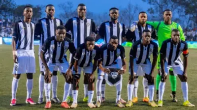 Abakinnyi b'ikipe ya APR FC yo mu Rwanda bahagaze mu kibuga barimo kureba muri 'camera'. Bambaye imyenda y'umweru n'umukara, mu gihe umunyezamu wayo yambaye imyenda y'umuhondo.