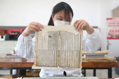 一個女生身著白褂，舉起一頁古籍文稿。