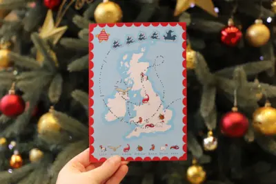 A map of the United Kingdom with a Christmas-themed design, showing a trail of Santa’s sleigh and various holiday icons such as reindeer, robins, and other animals, held in front of a decorated Christmas tree with ornaments