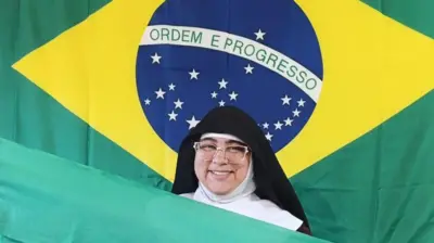 Madre Maria Rafaela, com vestes de freira, posa com bandeira do Brasil ao fundo