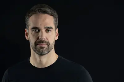 Eduardo Leite usa uma camisa preta e olha para a câmera