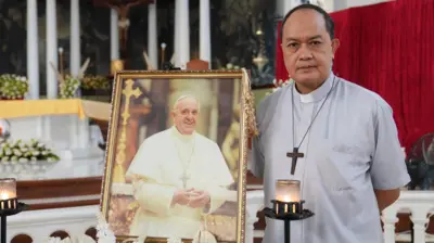 Cardinal Pablo Virgilio David standing shirt next to a photo of Pope Francis inside a cathedral.