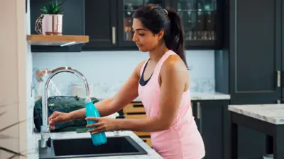 Woman filling water bottle at a kitchen tap