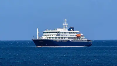 El crucero MV Hondius anclado frente al puerto de Praia, la capital de Cabo Verde, el 3 de mayo de 2026. Es una embarcación de gran tamaño, de color azul y blanco. 