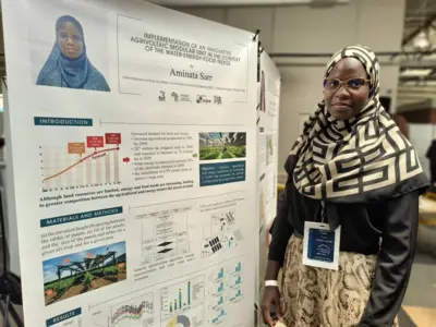 Aminata Sarr est debout à côté d'une affiche sur laquelle il y a beaucoup d'écritures.