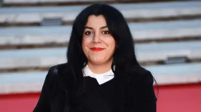 Marjane Satrapi siyah ceketle kameraya gülümserken