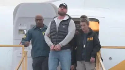 Ryan Wedding es escoltado por dos agentes del FBI mientras desciende de un avión