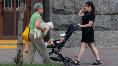 матір з дитиною у візочку і пенсіонерка з собачкою на вулицях Києва