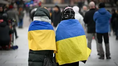 Женщины в зимних куртках, обернутые в украинские флаги