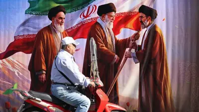 Homem de motocicleta em frente a um cartaz publicitário com as imagens do fundador da Revolução Islâmica e ex-líder supremo do Irã, o aiatolá Ruhollah Khomeini (esq.); do ex-líder supremo do Irã, Ali Khamenei (centro); e do atual líder supremo, Mojtaba Khamenei, em uma rua de Teerã, no dia 3 de julho de 2026