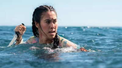 A woman in the water holding a knife, and looking to her right