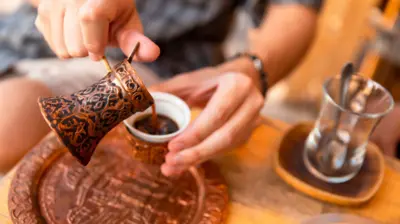 bakır cezveden bir fincana kahve boşaltan bir el ve kenarda bir çay bardağı