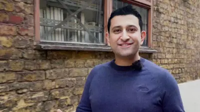 Actor and presenter Waseem Mirza stands in front of a wall wearing a blue jumper.