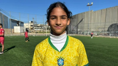 Una niña palestina mira a cámara, está en un campo de fútbol y viste la camiseta de la selección de Brasil