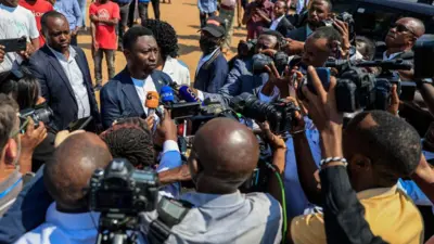 Umurwi w'abanyamakuru benshi mu Rwanda bari mw'ibarabara babaza umukandida, umukuru w'umugambwe 'Democratic Green Party', Frank Habineza, inyuma yo gutorera ku Kimironko i Kigali, kw'igenekerezo rya 15 Mukakaro (7) mu 2024. (Ifoto mbarankuru yo mu bubiko)
