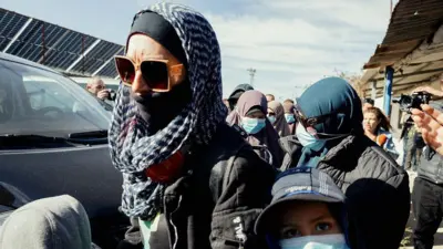 A woman in a headscarf and dark glasses with other women in headscarves and faces masks behind her.