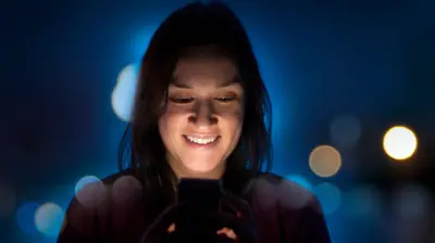 elindeki akıllı telefon ekranına bakan bir kadın gülümsüyor