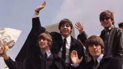 Os Beatles acenam ao desembarcarem de um avião em 1964.