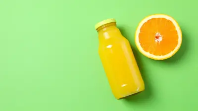 Bir şişe portakal suyu yatay yeşil zeminde yanında yarım portakal var. 