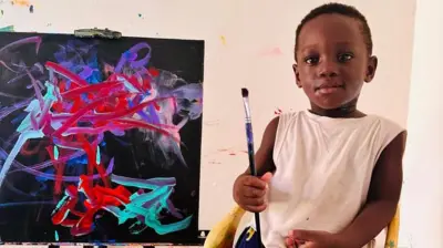 Un enfant en bas âge tenant un pinceau devant un tableau
