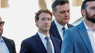 Mark Zuckerberg cercado por três seguranças enquanto caminha em direção a um tribunal de Los Angeles, vestindo um blazer azul-marinho, gravata cinza e camisa branca.