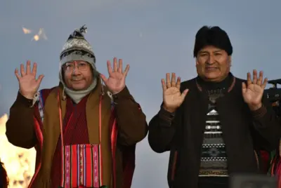 Luis Arce e Evo Morales com as mãos levantadas em cerimônia 