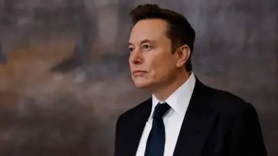 Elon Musk vestindo um terno preto, camisa branca e gravata preta olhando para longe
