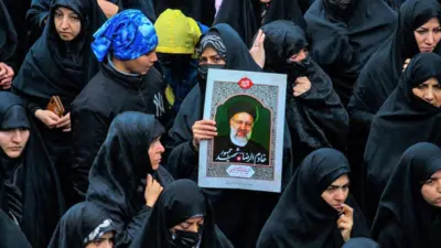 İran'da Reisi'nin cenazesinde bir grup kadın onun afişini tutuyor