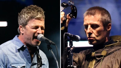 Noel (à esquerda) e Liam Gallagher (à direita), da banda Oasis. Noel, com uma camisa jeans azul, está diante de um microfone, provavelmente cantando ou se dirigindo ao público. Liam, com uma jaqueta escura, ergue um pandeiro acima da cabeça com uma das mãos.