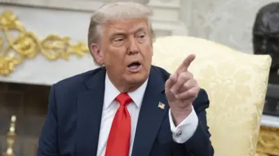 Donald Trump points while sitting in the Oval Office.