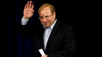 Mohammad Bagher Ghalibaf wearing a white shirt and black suit, waving and standing against a black background.