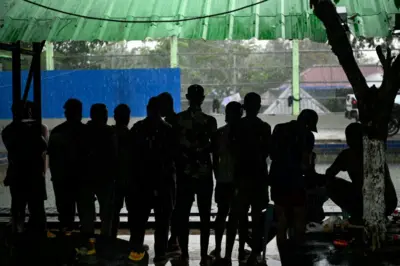 በታይላንድ መጠለያ ክፍል ጨለማ ውስጥ ተደርድርው ወደ ውጭ እያዩ የቆሙ ወንዶች