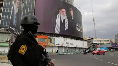 तेहरान के एक चौराहे पर खड़ा सुरक्षा बल और पीछे लगा अली ख़ामेनेई का पोस्टर