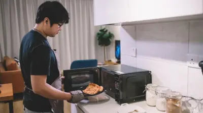 一名年轻男子从微波炉里拿出一片披萨